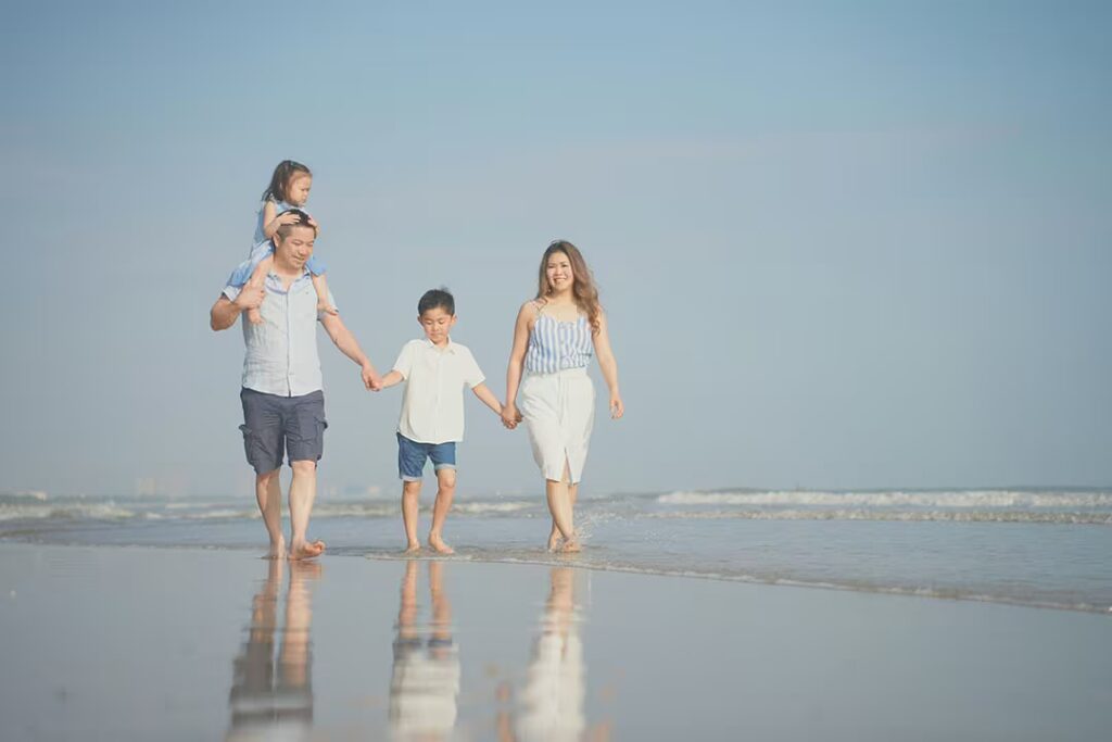 Family walking on a sandy beach near the water's edge.